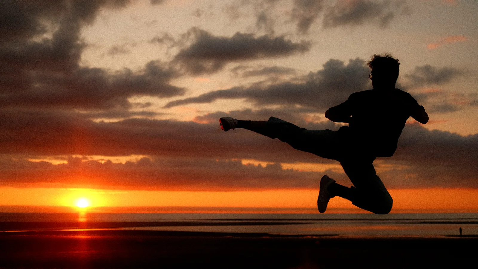 A martial artist performing a flying side kick silhouetted against a sunset sky